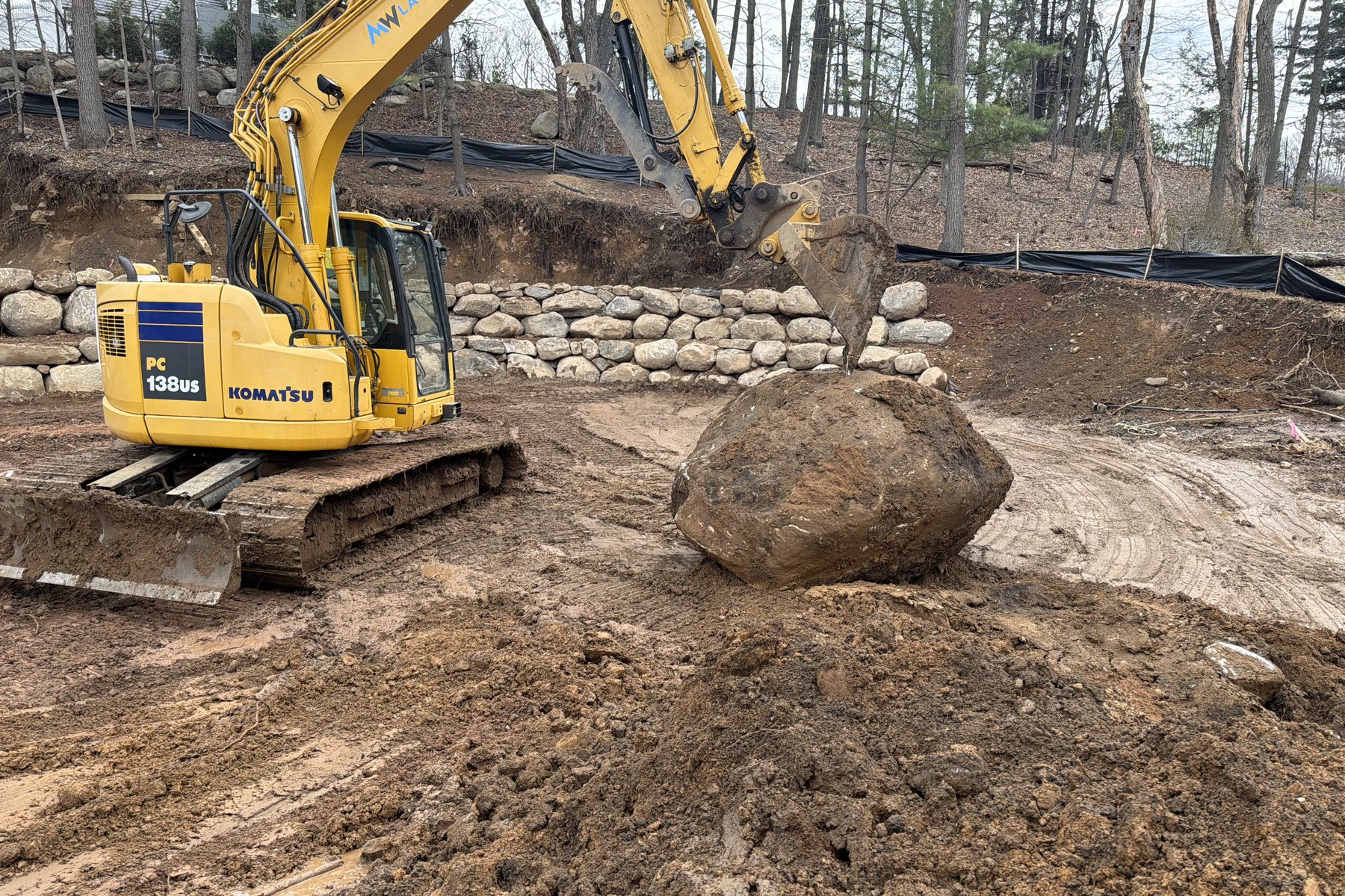 MW Landworks branded excavator placing boulder for retaining wall